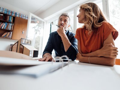 Unterlagen zur Heizungsmodernisierung liegen auf dem Tisch, zwei Personen beraten sich in einem modernen Büro.