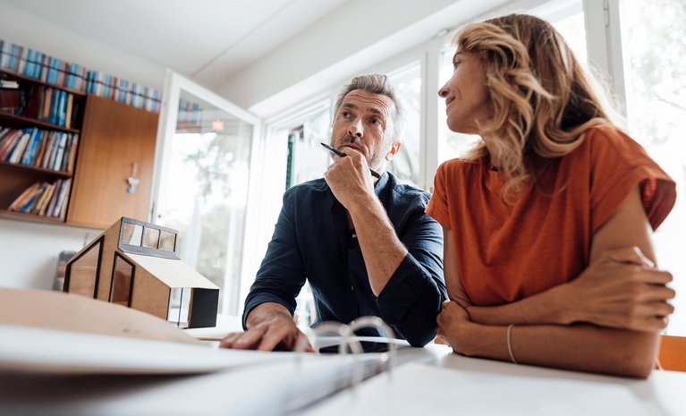 Unterlagen zur Heizungsmodernisierung liegen auf dem Tisch, zwei Personen beraten sich in einem modernen Büro.