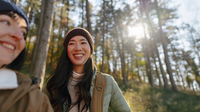 Zwei lächelnde Frauen im sonnigen Wald, symbolisieren zugänglichen Klimaschutz und Teilnahme an der Energiewende.