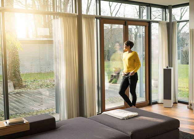 Gasverbrauch Einfamilienhaus: Frau steht am Fenster, Sonnenlicht, moderner Wohnraum, große Heizung, Energieeffizienz im Fokus.