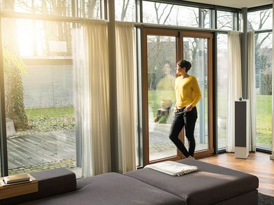 Gasverbrauch Einfamilienhaus: Frau steht am Fenster, Sonnenlicht, moderner Wohnraum, große Heizung, Energieeffizienz im Fokus.