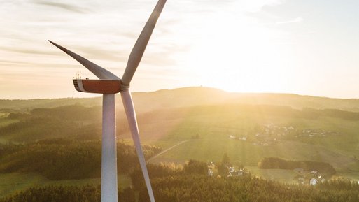 Windkraftanlage unter der aufgehenden Sonne, umgeben von Wäldern und Feldern. Hervorhebung von ENTEGAs Engagement für erneuerbare Energien.
