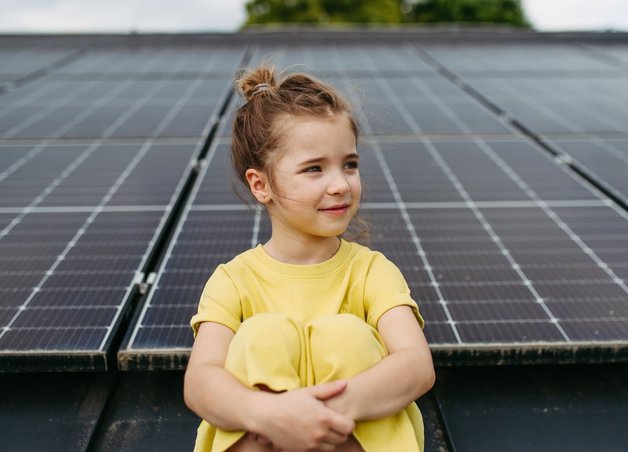 Ein Mädchen in gelbem Kleid sitzt vor Solarmodulen. Sie stehen als Symbol für die Zukunft der Energie und den Kohleausstieg.