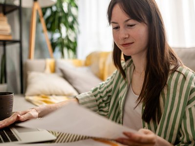 Junge Frau prüft Unterlagen und tippt am Laptop, bereitet sich darauf vor, ihren Stromanbieter zu kündigen, gemütliche Wohnumgebung.