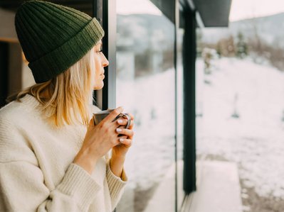 Bild zeigt eine Frau vor winterlichem Fenster als Symbolbild zum Thema