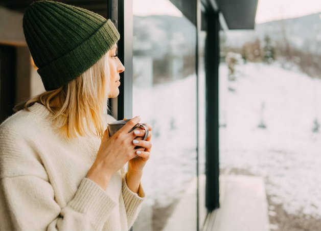 Bild zeigt eine Frau vor winterlichem Fenster als Symbolbild zum Thema