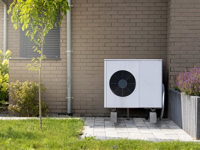 Wärmepumpe aufstellen: Moderne Wärmepumpe vor Klinkerhaus, eingebettet in gepflegten Garten, zeigt umweltfreundliche Energieversorgung.