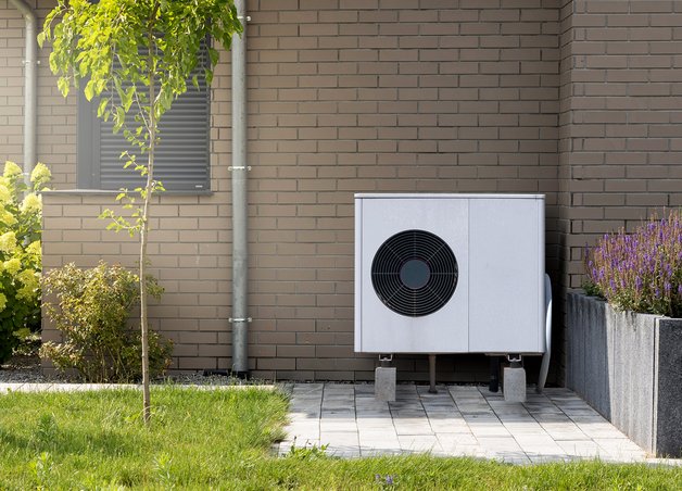 Wärmepumpe aufstellen: Moderne Wärmepumpe vor Klinkerhaus, eingebettet in gepflegten Garten, zeigt umweltfreundliche Energieversorgung.