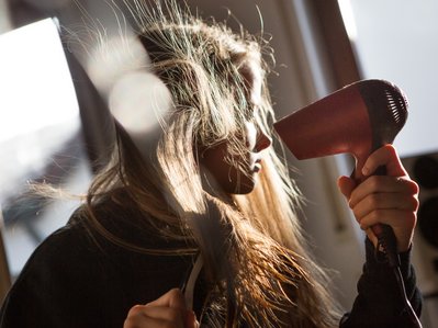 Bild zeigt eine Frau, die ihre Haare föhnt – Thema: Energieverbrauch pro Person.
