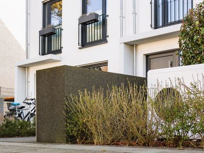 Beispiel der Aufstellung einer Wärmepumpe vor einem Wohnhaus: seitlich am Eingang von Hecken umgeben.