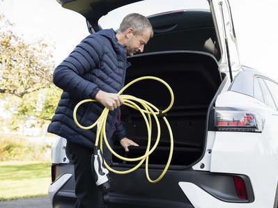 Bild zeigt einen Mann, der sein Elektroauto lädt und sich während der Ladezeit mit seinem Handy beschäftigt.