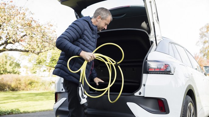 Bild zeigt einen Mann, der sein Elektroauto lädt und sich während der Ladezeit mit seinem Handy beschäftigt.