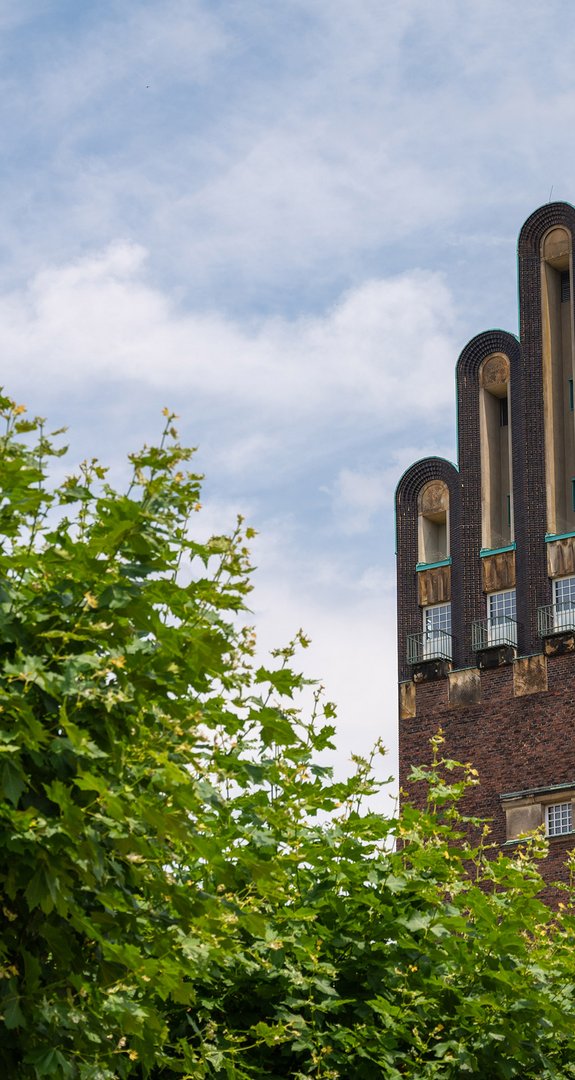 Hochzeitsturm in Darmstadt unter blauem Himmel, umgeben von Bäumen. Informationen und Angebote zur Kündigung in der Stadt Darmstadt.