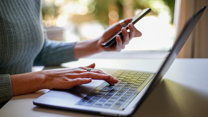 Person tippt am Laptop und hält in der anderen Hand ein Smartphone. Symbolisiert Informationen zur Änderung der Bankverbindung für ENTEGA Kunden.
