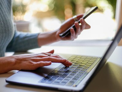 Person tippt am Laptop und hält in der anderen Hand ein Smartphone. Symbolisiert Informationen zur Änderung der Bankverbindung für ENTEGA Kunden.