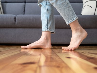 Füße laufen barfuß über warmen Holzboden vor Sofa, Stromverbrauch Fußbodenheizung als zentrales Thema für Wohnkomfort.