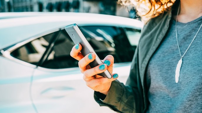 Bild illustriert, wie man erfolgreich eine Mitfahrgelegenheit finden kann und zeigt eine Frau, die etwas in ihr Handy tippt