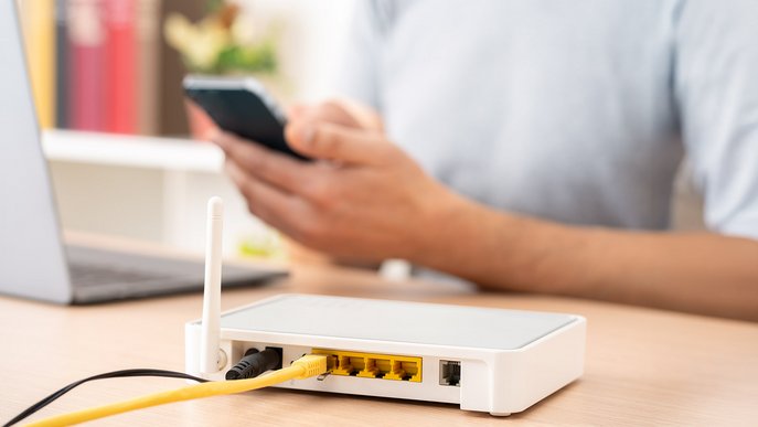 Nahaufnahme eines weißen Routers, Person hält ein Smartphone. Symbolisiert Informationen von ENTEGA zur Behebung von Internet-Problemen mit der FRITZ!BOX.
