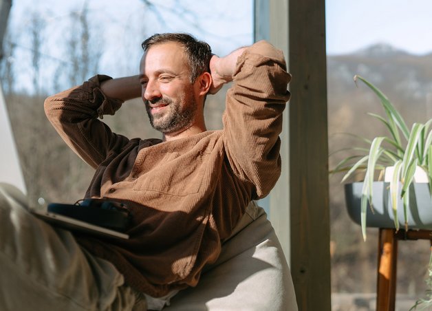 Mann arbeitet entspannt mit Laptop vor Fenster, Thema: Was kostet Strom bei Homeoffice und digitalem Alltag.