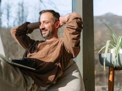 Mann arbeitet entspannt mit Laptop vor Fenster, Thema: Was kostet Strom bei Homeoffice und digitalem Alltag.