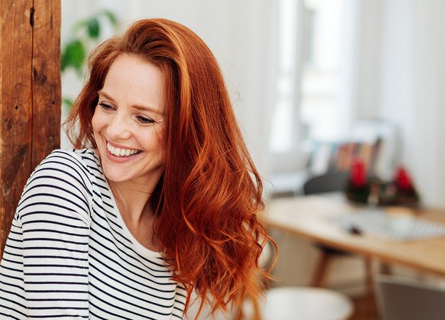 Rothaarige Frau in einem Wohnzimmer steht für Stromverbrauch Singlehaushalt.
