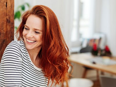 Rothaarige Frau in einem Wohnzimmer steht für Stromverbrauch Singlehaushalt.