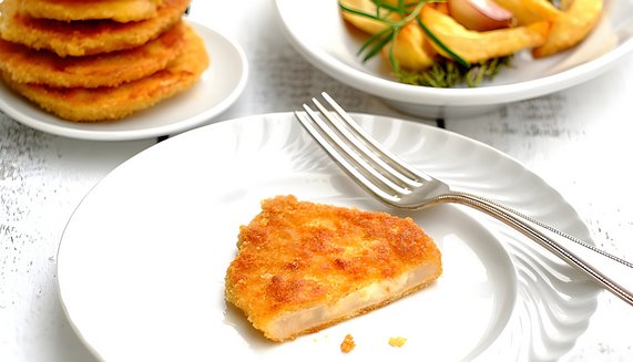 Knuspriges Sellerieschnitzel auf einem weißen Teller, daneben ein Teller mit Kartoffelspalten und Rosmarin, herbstliche Mahlzeit.