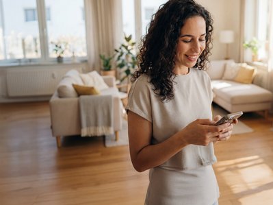 Frau mit Smartphone in heller, modernen Wohnung, informiert sich über den Tarif Dynamischer Ökostrom; nachhaltiges Leben im Alltag.