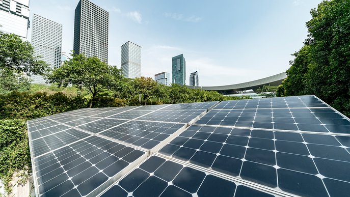 Photovoltaik-Panels in einem grünen Bereich mit modernen Hochhäusern im Hintergrund, verbindet nachhaltige Technik mit urbaner Landschaft.