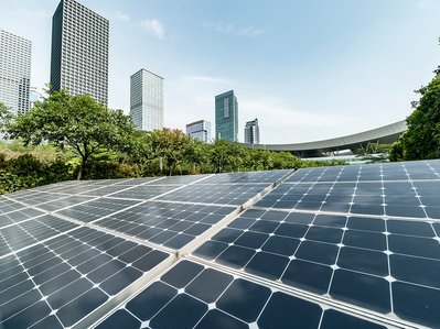 Photovoltaik-Panels in einem grünen Bereich mit modernen Hochhäusern im Hintergrund, verbindet nachhaltige Technik mit urbaner Landschaft.