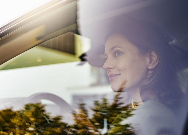 Eine Frau sitzt am Steuer hinter spiegelnder Seitenscheibe. Symbolbild für Elektroauto Nachteile wie Ladepause und Planung.