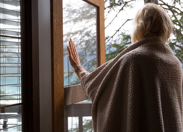 Frau im warmen Pullover öffnet ein Fenster, umgeben von Natur, demonstriert „Richtig lüften“ für frische Luft und gesundes Raumklima.