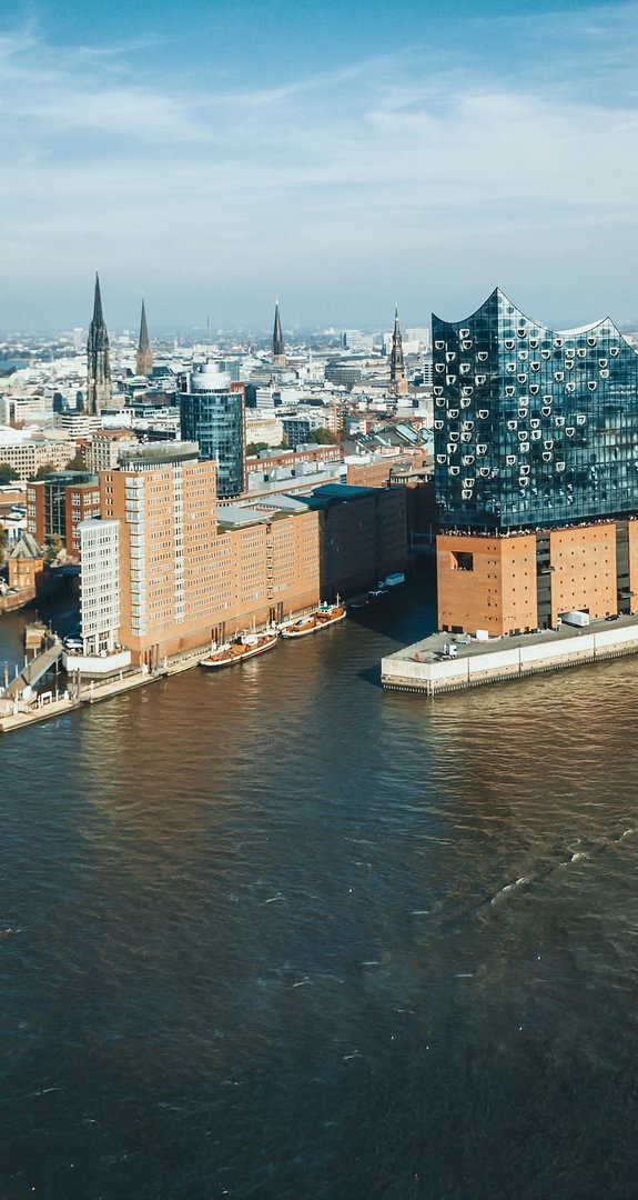 Luftaufnahme der Hamburger Elbphilharmonie, umgeben von Hafen und Stadtzentrum. Zeigt Architekturikone und lebendigen Schiffsverkehr des Hafens.