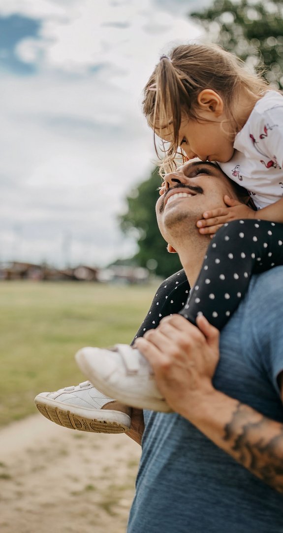 Lächelnder Vater mit Kind auf den Schultern, in grüner Umgebung, steht für umweltbewusste Energieentscheidungen.