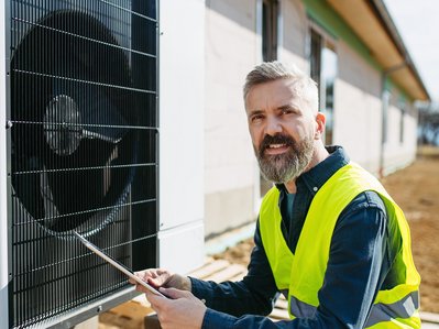 Bild zeigt einen Mann, der vor einer Wärmepumpe steht – Thema: Möglichkeiten und Herausforderungen der Innenaufstellung von Wärmepumpen.