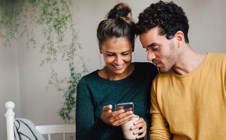 Zwei Freunde sitzen zusammen und freuen sich über die Einlösung einer Empfehlungsprämie auf dem Smartphone.