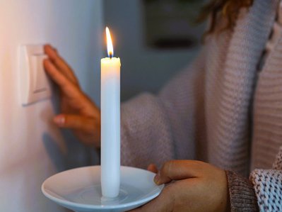 Eine Person mit Kerze in der Hand greift zum Lichtschalter an der Wand. Szene bei Stromabschaltung mit improvisiertem Licht.