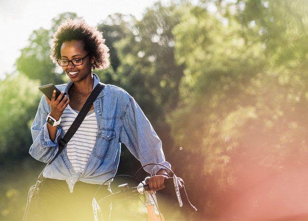 Nachhaltig kommunizieren: Junge Person schiebt Fahrrad im Park und spricht ins Smartphone, Fokus auf umweltfreundliche Mobilität und digitale Kommunikation.
