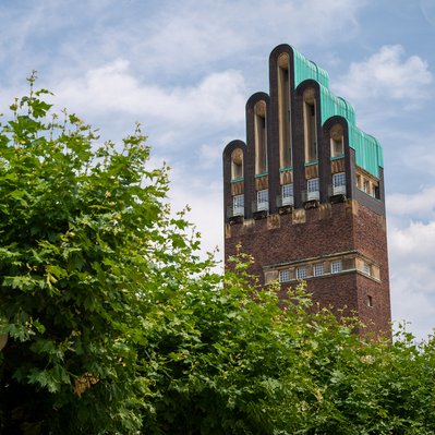 Hochzeitsturm in Darmstadt unter blauem Himmel, umgeben von Bäumen. Bekräftigt Darmstadts Engagement für umweltfreundliche Energie mit Fernwärme.