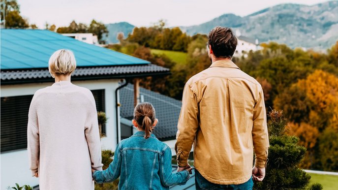 Bild zum Thema PV-Anlage finanzieren: Eine Familie steht vor einem Einfamilienhaus mit Solaranlage