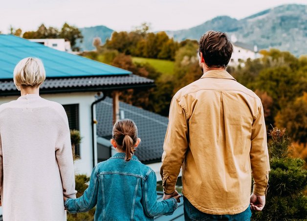 Bild zum Thema PV-Anlage finanzieren: Eine Familie steht vor einem Einfamilienhaus mit Solaranlage