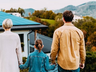 Bild zum Thema PV-Anlage finanzieren: Eine Familie steht vor einem Einfamilienhaus mit Solaranlage
