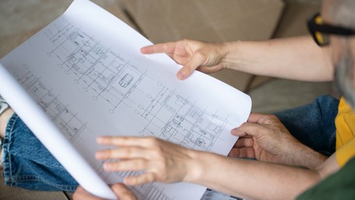 Hände zeigen auf technische Zeichnung eines Hauses. Symbolisiert Planung und gezielte energetische Verbesserungen.