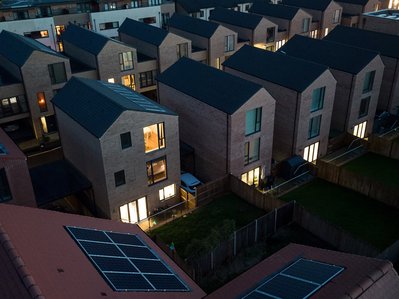 Moderne Wohnsiedlung bei Dämmerung, viele Fenster beleuchtet, Solarpanels sichtbar; Thema Stromverbrauch weltweit und Energiewende.