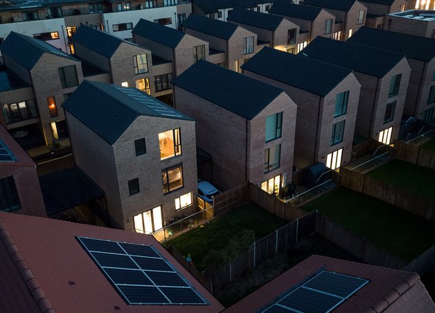 Moderne Wohnsiedlung bei Dämmerung, viele Fenster beleuchtet, Solarpanels sichtbar; Thema Stromverbrauch weltweit und Energiewende.
