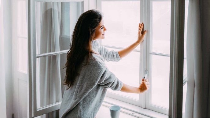 Bild zeigt eine Frau, die ein Fenster öffnet