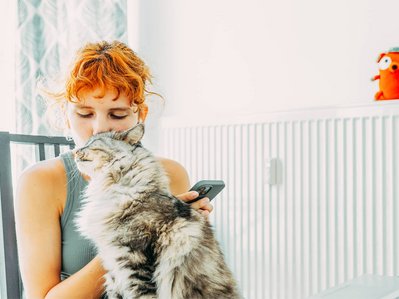 Bild zeigt eine Frau, kuschelnd mit einer Katze vor einem Heizkörper, Symbolbild zum Thema „Gasheizung“