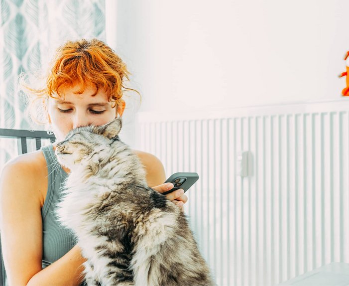 Bild zeigt eine Frau, kuschelnd mit einer Katze vor einem Heizkörper, Symbolbild zum Thema „Gasheizung“