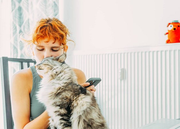 Bild zeigt eine Frau, kuschelnd mit einer Katze vor einem Heizkörper, Symbolbild zum Thema „Gasheizung“