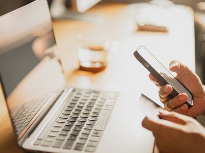 Detailansicht von Smartphone und Karte auf Schreibtisch mit Laptop, symbolisiert unkomplizierte Anpassung der Bankdaten bei ENTEGA.